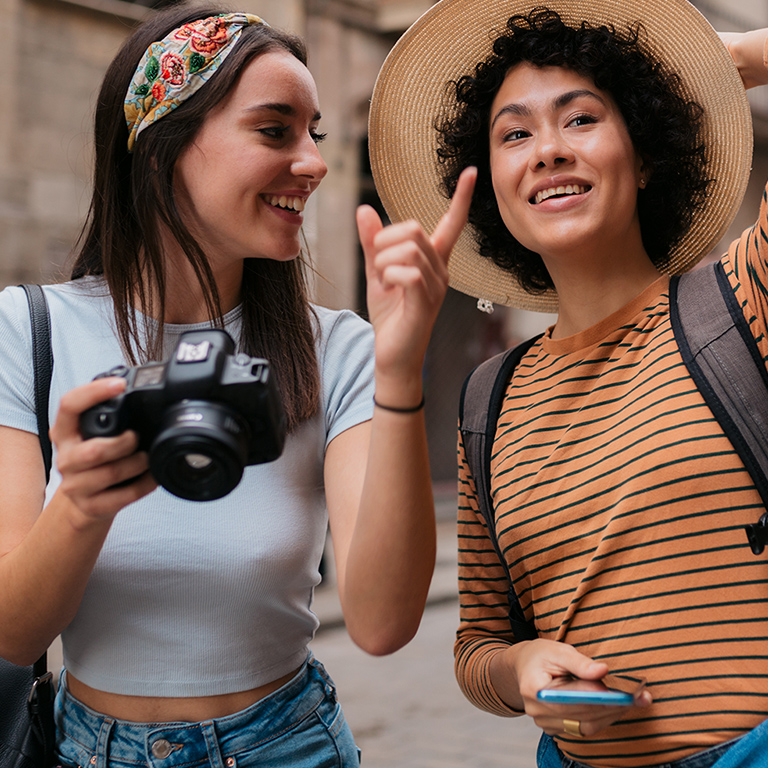 Young diverse lesbian couple enjoying their vacation together, exploring a foreign European city holding a photographic camera, bonding and having fun